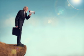 senior businessman yelling through a loudhailer from a cliff edge