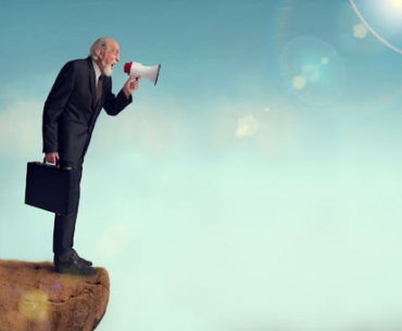 senior businessman yelling through a loudhailer from a cliff edge